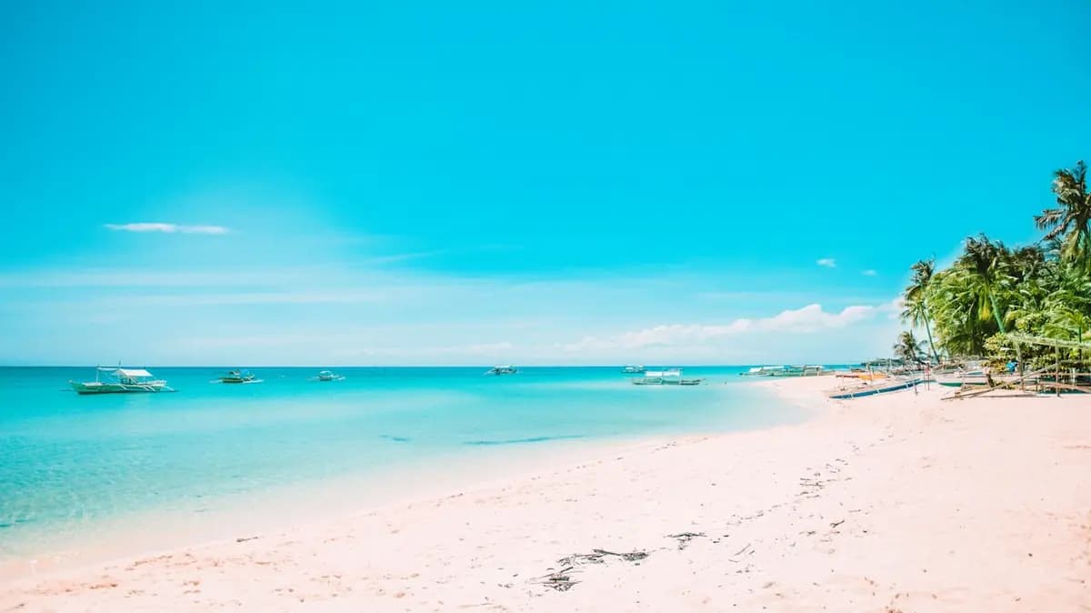 Bãi biển cát trắng nước biển xanh ngọc, thuyền neo gần bờ dưới trời nắng